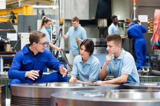 Three factory workers in workspace talking.